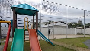 Un parque infantil con toboganes y una estructura para escalar, rodeado por una cerca.