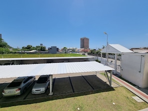 A parking area with two cars, a covered waiting area, and a tall building in the background. - Curta Praia do Quilombo - Palladium  (Penha)
