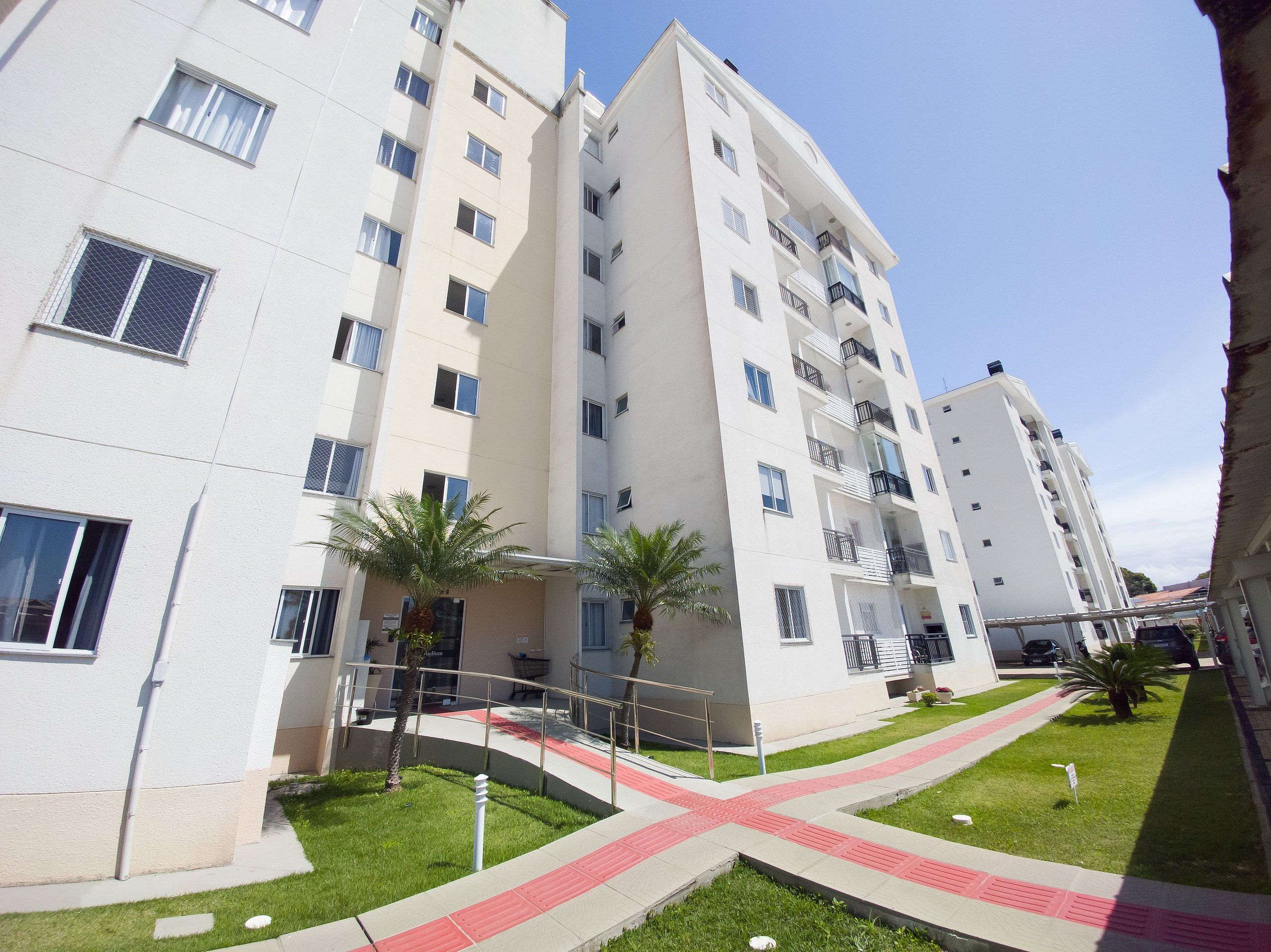 Un edificio residencial de varios pisos con balcones, un patio ajardinado y un sendero peatonal.