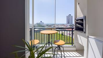 A balcony with two small tables and chairs, a potted plant, and a view of a cityscape.