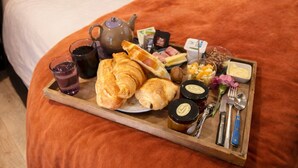 A neatly made bed with a tray of breakfast items including croissants, a teapot, and condiments.