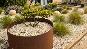 A house with a stone facade, a garden with a large planter, and a gravel pathway.