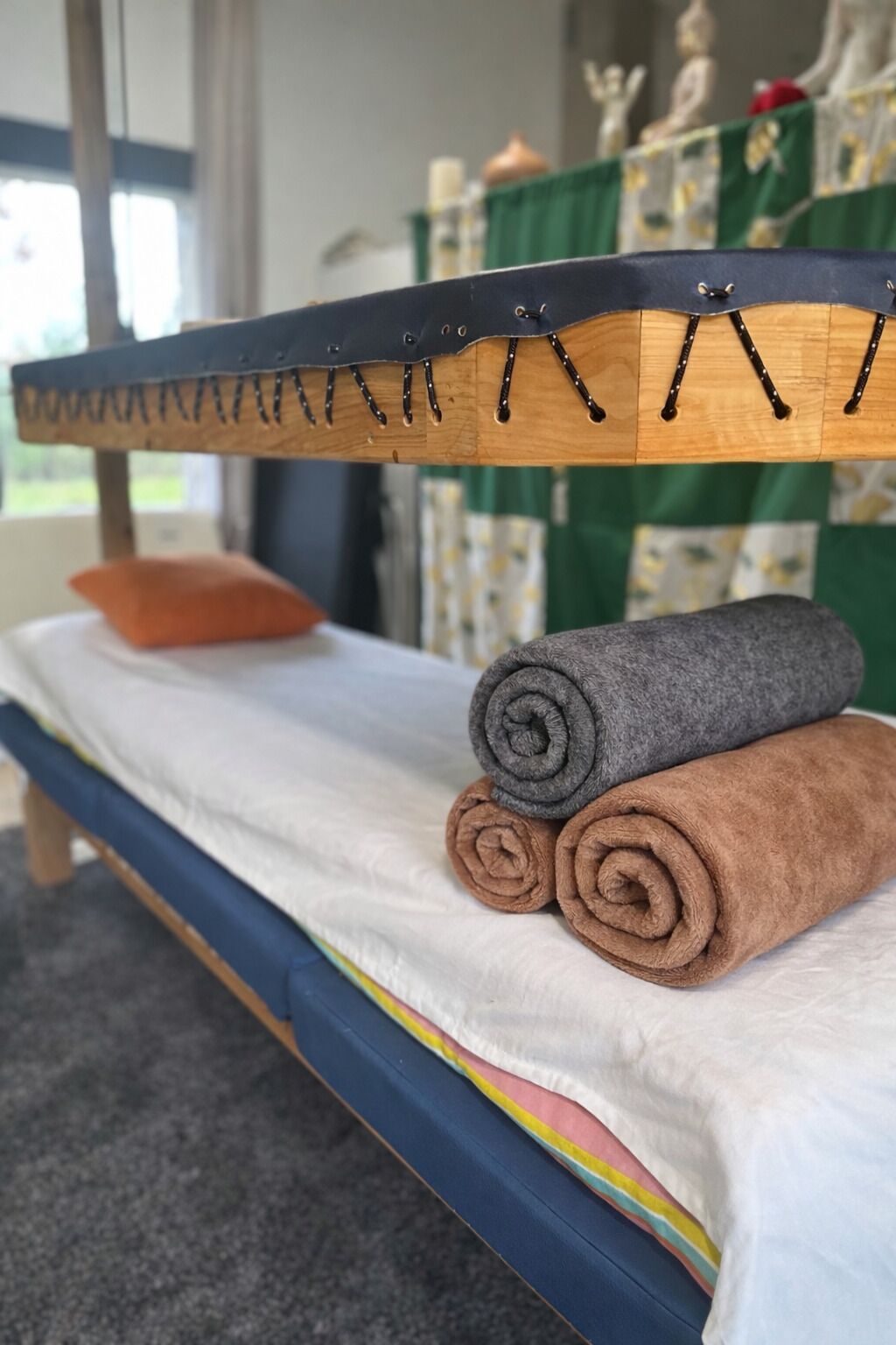 Un lit avec une tête de lit en bois, un matelas blanc et des serviettes roulées de couleur marron et grise.