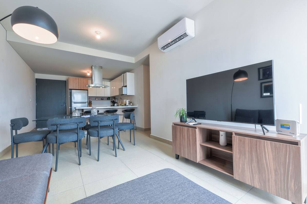 A modern apartment with a dining area, kitchen, and a large TV.