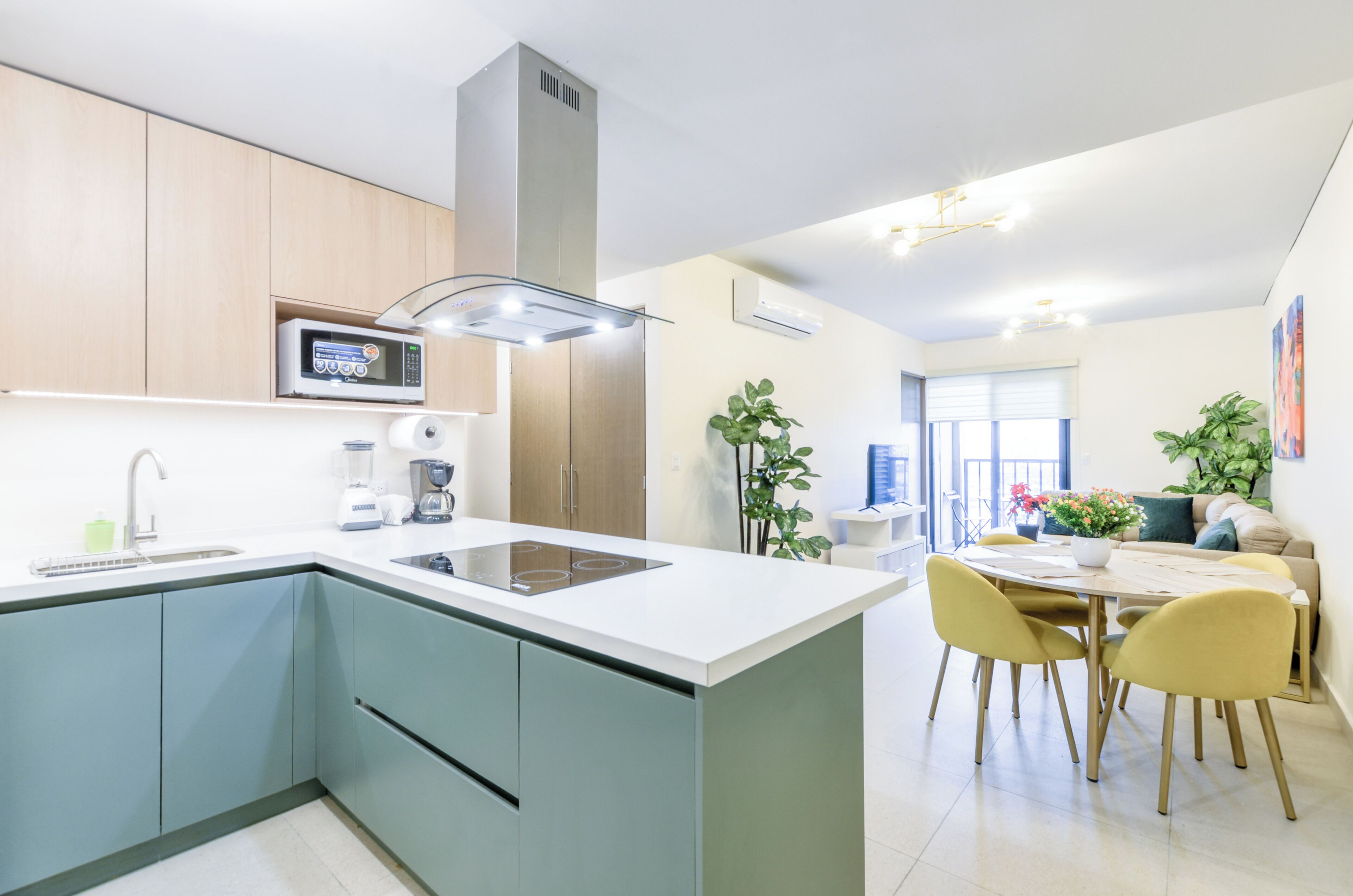 A modern kitchen with a central island, built-in appliances, and a dining area with yellow chairs.