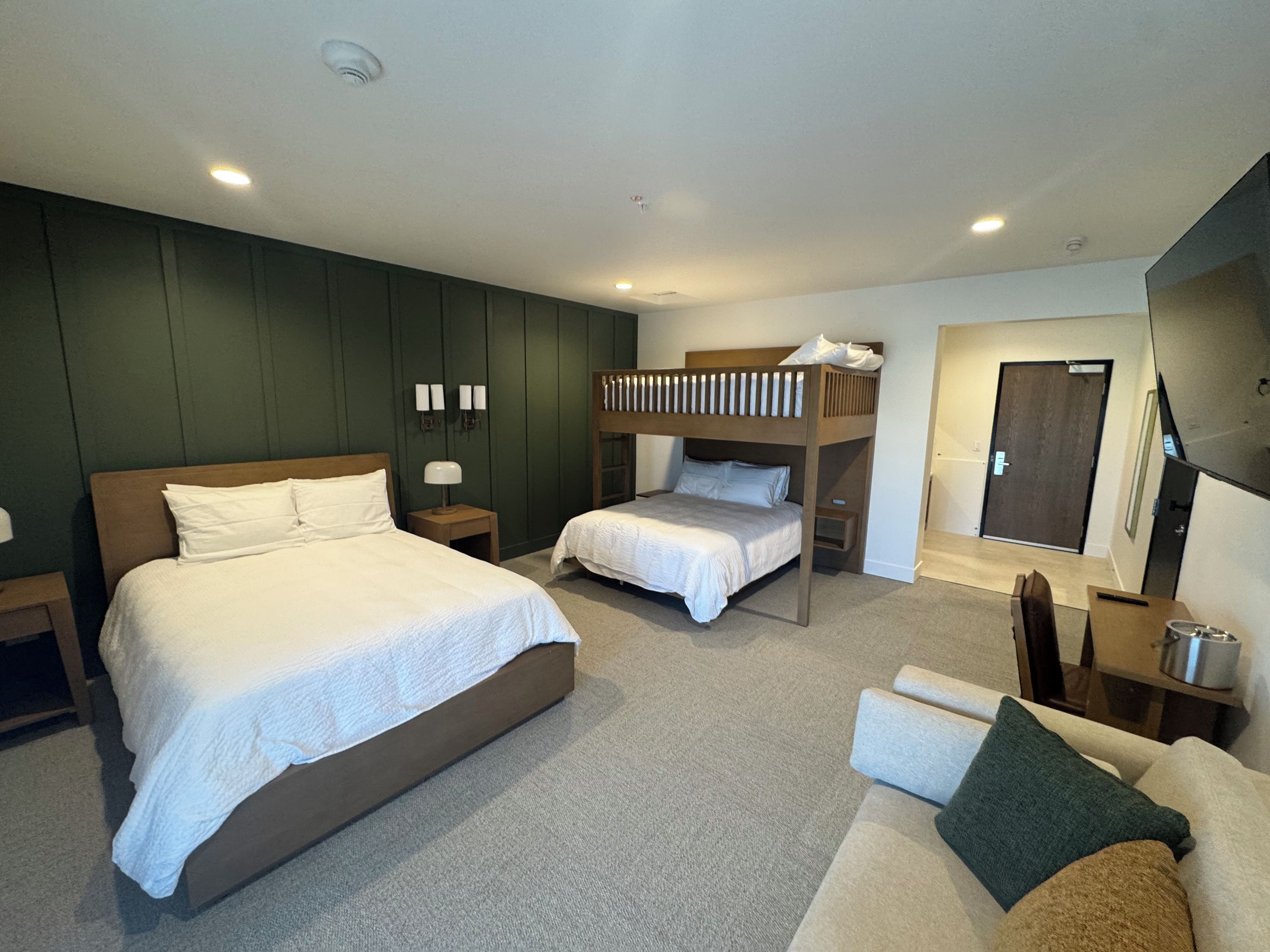 A hotel room with a large bed, a smaller bed, a sofa, a desk, and a mirror.