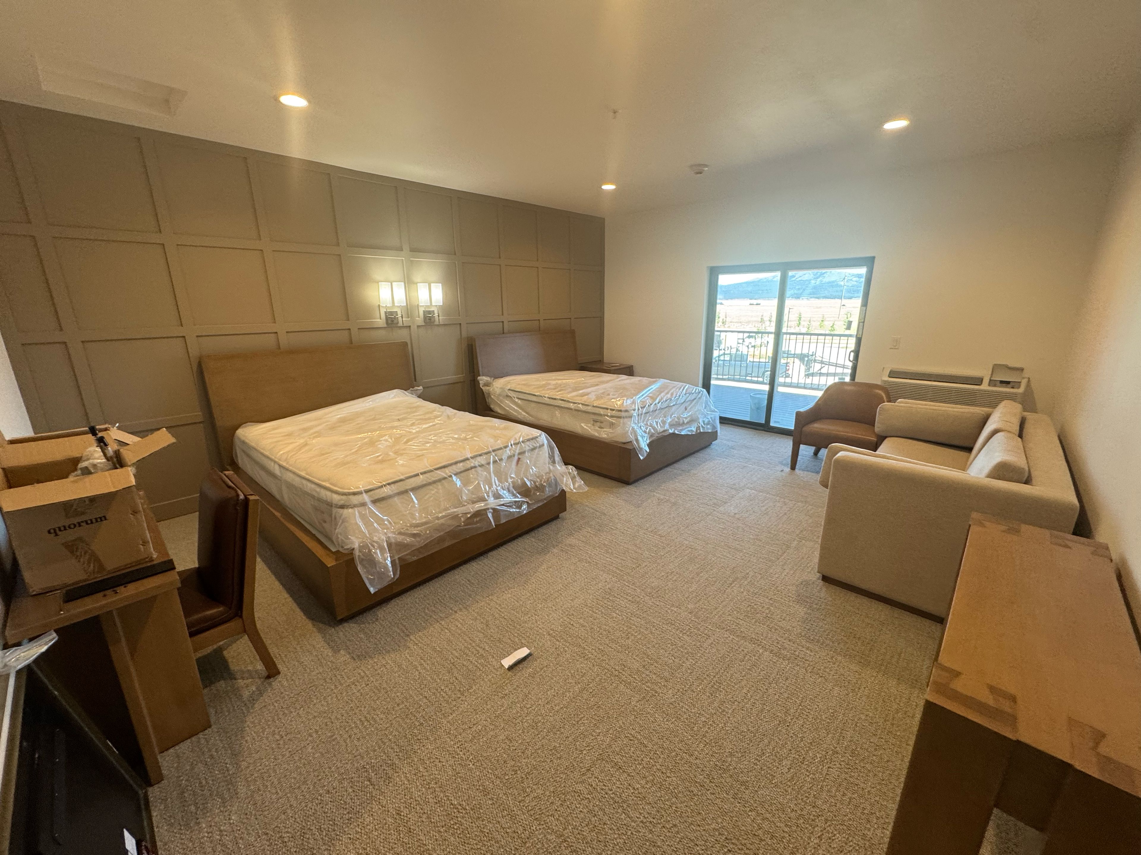 Habitación de hotel con dos camas, un sofá, un escritorio y un ventanal grande.