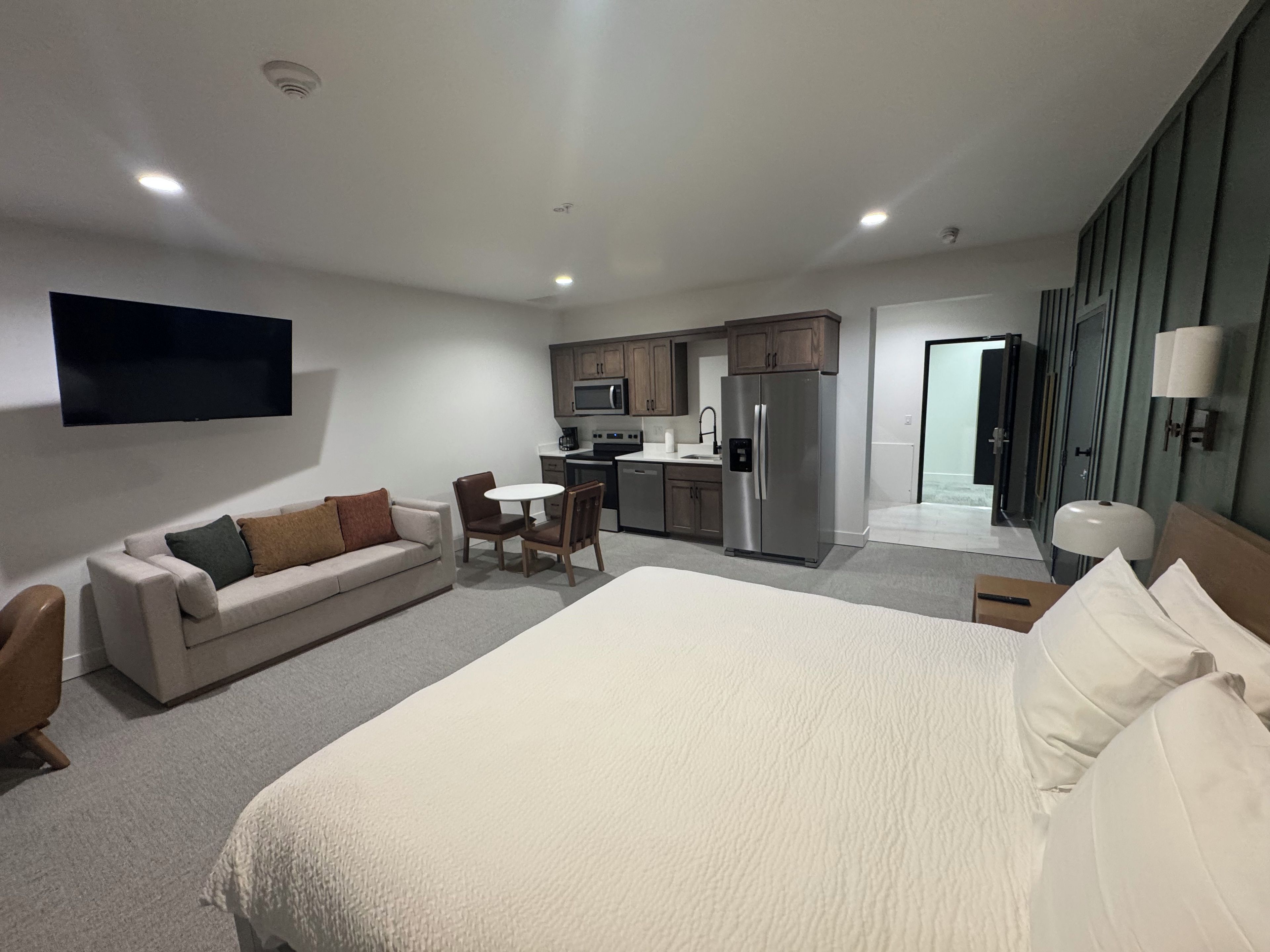 Une chambre d’hôtel comprenant un lit, un canapé, une table à manger avec des chaises, un coin cuisine et un téléviseur à écran plat fixé au mur.