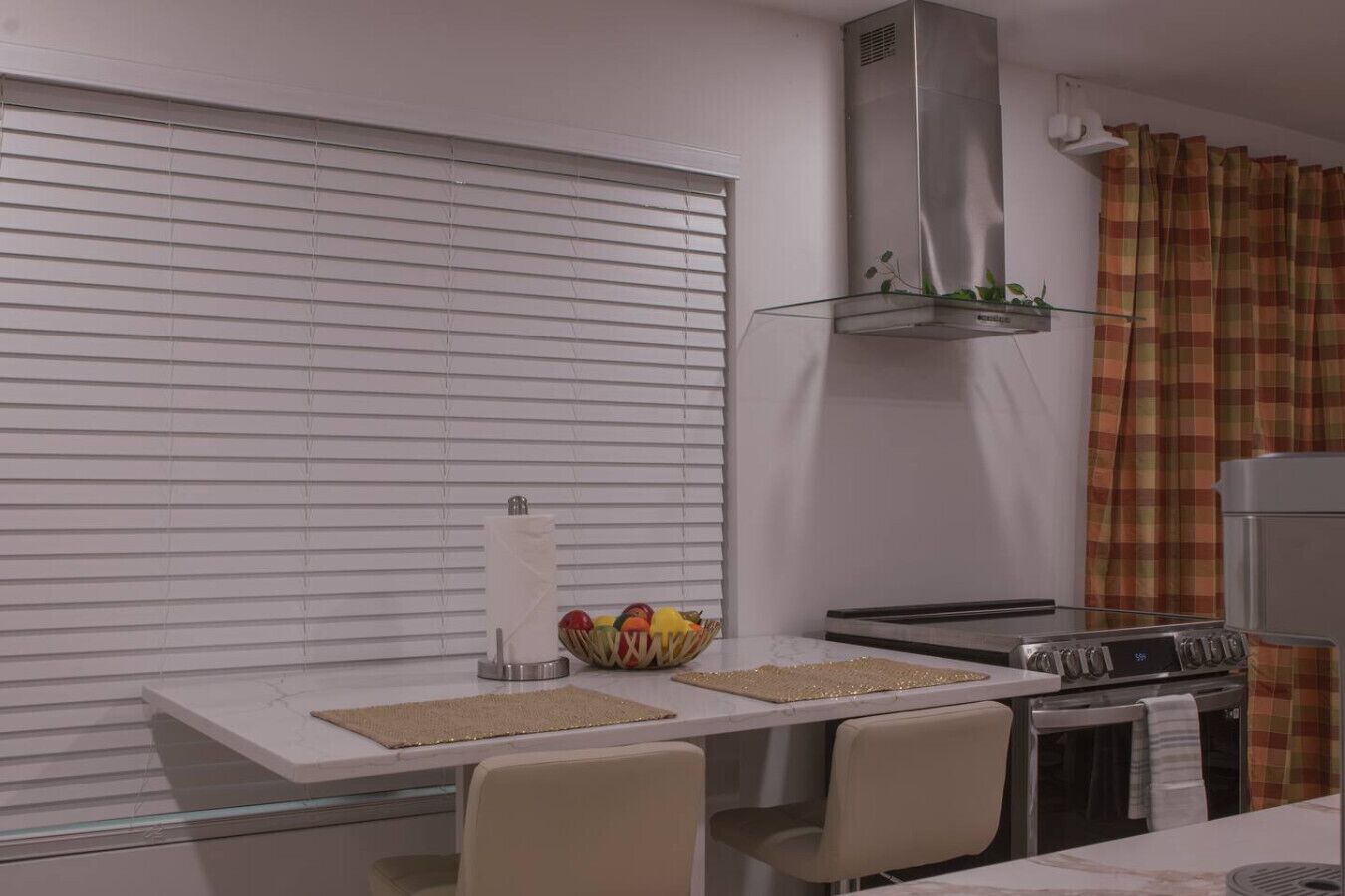 Une cuisine moderne dotée d’une cuisinière intégrée, d’une hotte en acier inoxydable et d’une fenêtre avec des stores.