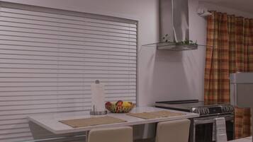 Une cuisine moderne dotée d’une cuisinière intégrée, d’une hotte en acier inoxydable et d’une fenêtre avec des stores.