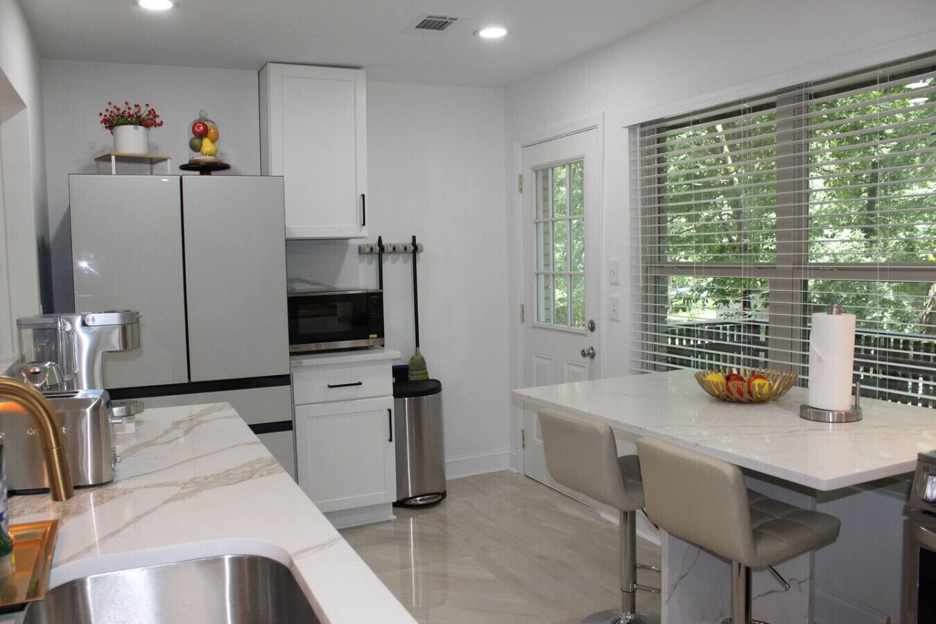 A modern kitchen with white cabinetry, a built-in microwave, a stainless steel sink, and a window with blinds.