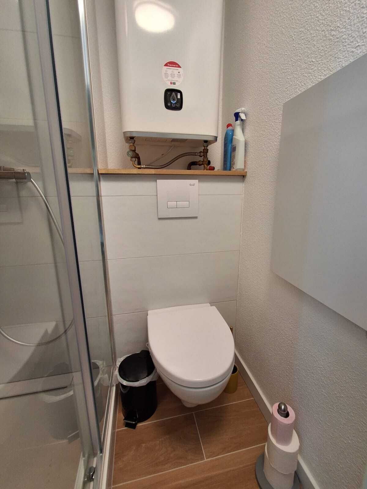 A bathroom with a toilet, a shower, and a wall-mounted heater.