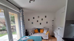 Een moderne woonkamer met een bank, een eettafel met snijplank, een keukenhoek en uitzicht op de omgeving.
