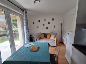 A modern living room with a sofa, a dining table with a cutting board, a kitchen area, and a view of the outdoors. - Appart' Pyrénées Nature, comfortable, with terrace and small garden (Esquièze-Sère)