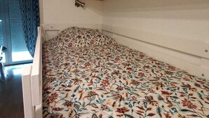 Een kleine kamer met een bed, een plank met boeken en een deur met gordijn.