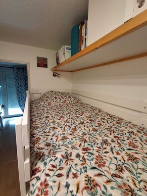 A small room with a bed, a shelf with books, and a door with a curtain. - Appart' Pyrénées Nature, comfortable, with terrace and small garden (Esquièze-Sère)