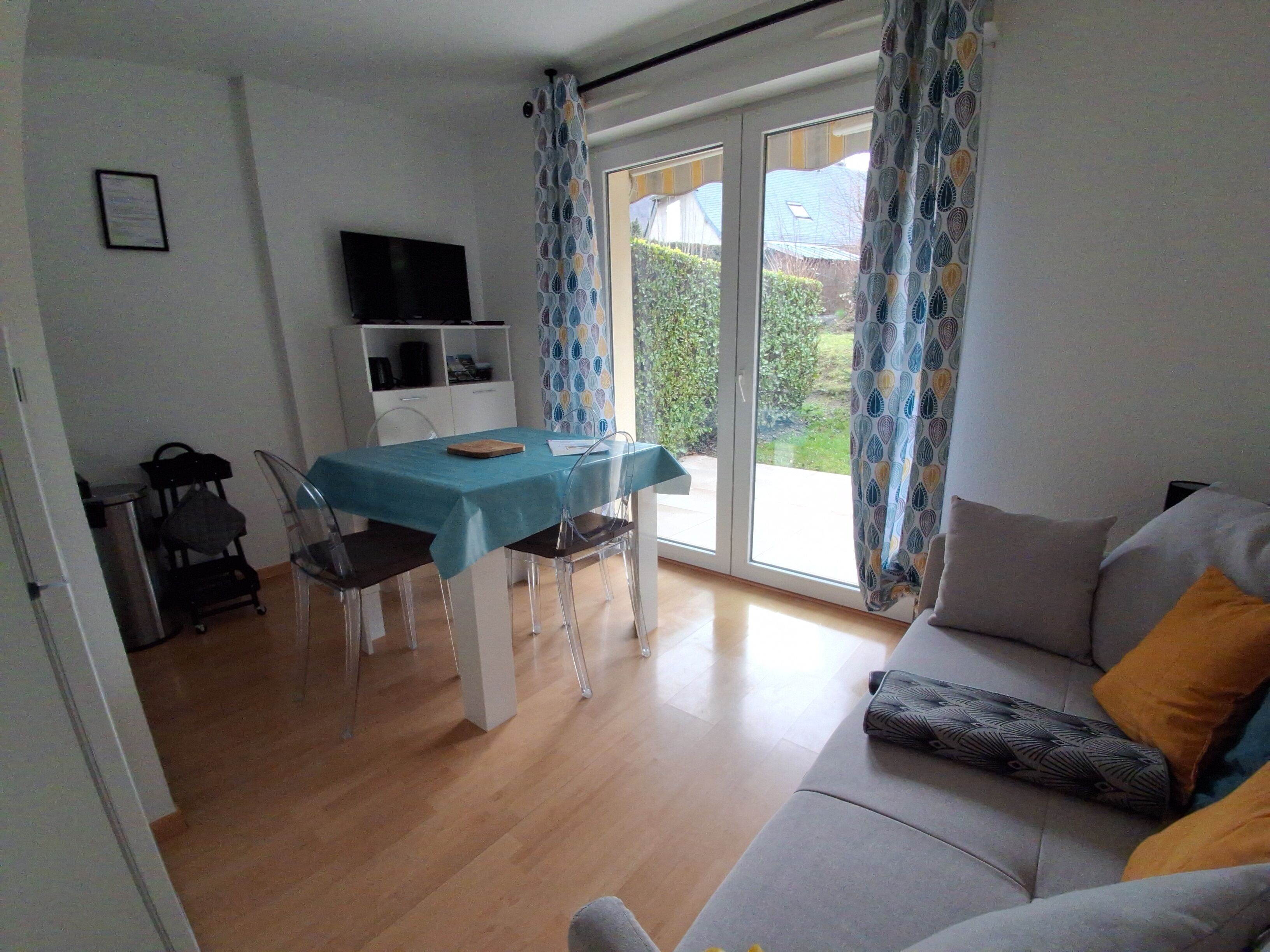 A dining area with a table and chairs, a sofa, and a television on the wall.