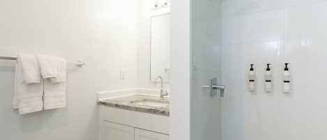 Un baño con lavamanos, espejo, toallero y ducha.