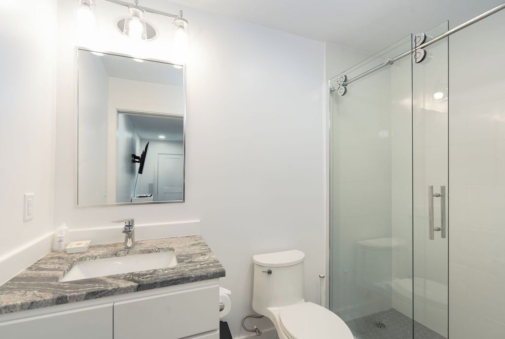 Een moderne badkamer met een marmeren wastafel, een toilet en een douche met glazen wanden.