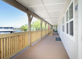 A covered porch with a wooden railing, a white exterior wall, and a clear view of the sky and trees.