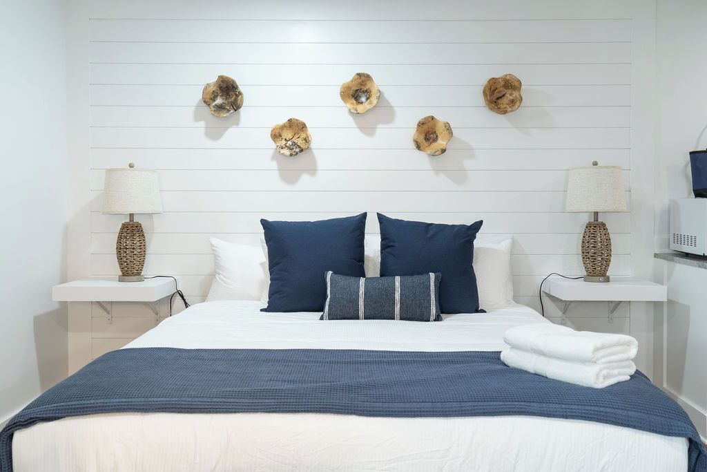 A neatly made bed with a blue and white color scheme, flanked by two bedside tables with lamps, and a wall-mounted decorative item above the bed.