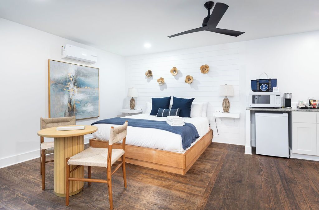 Un dormitorio con cama, mesitas de noche, un escritorio, una silla, ventilador de techo, microondas y un refrigerador pequeño.