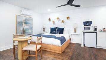 Un dormitorio con cama, mesitas de noche, un escritorio, una silla, ventilador de techo, microondas y un refrigerador pequeño.