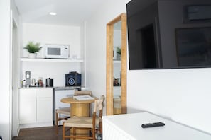 Habitación compacta con kitchenette, una mesa redonda con dos sillas, un espejo grande y un control remoto sobre una superficie blanca.