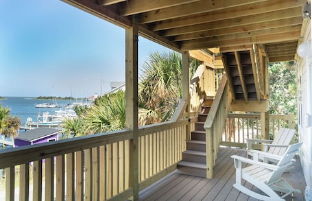 A wooden deck with a view of the marina and boats, a staircase, and two white rocking chairs.