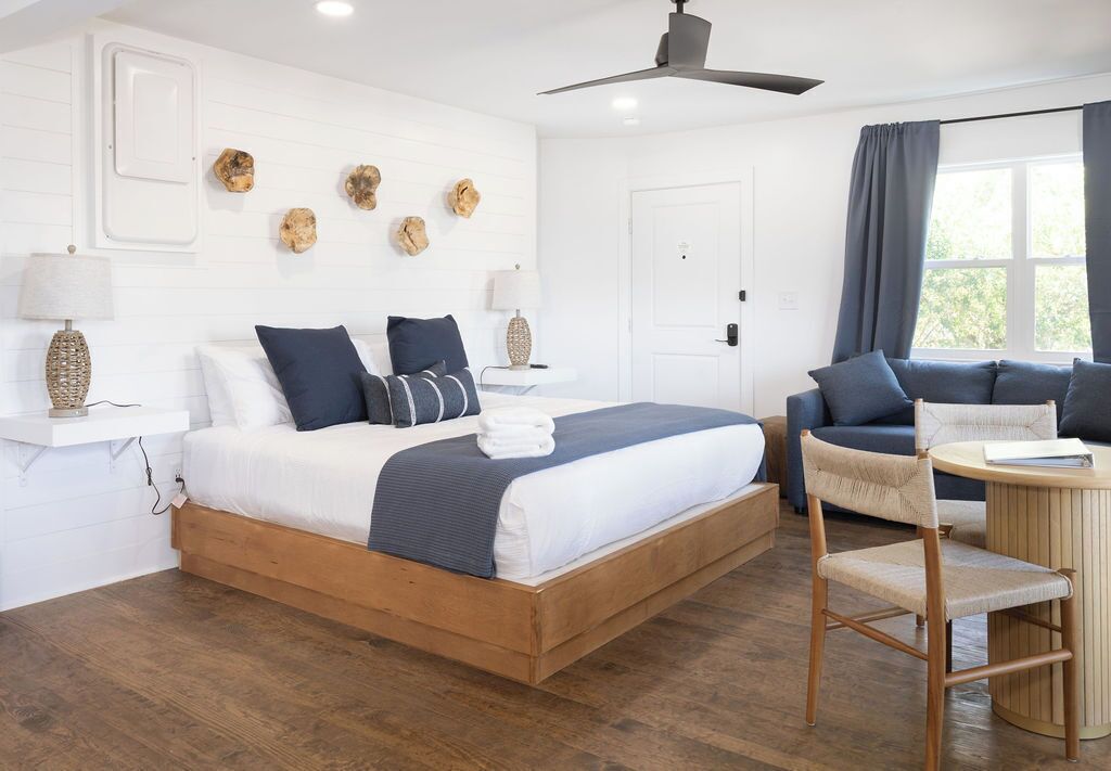 A bedroom with a wooden bed, a sofa, a chair, a round table, and a ceiling fan.