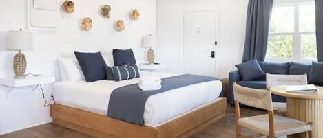 A bedroom with a wooden bed, a sofa, a chair, a round table, and a ceiling fan.