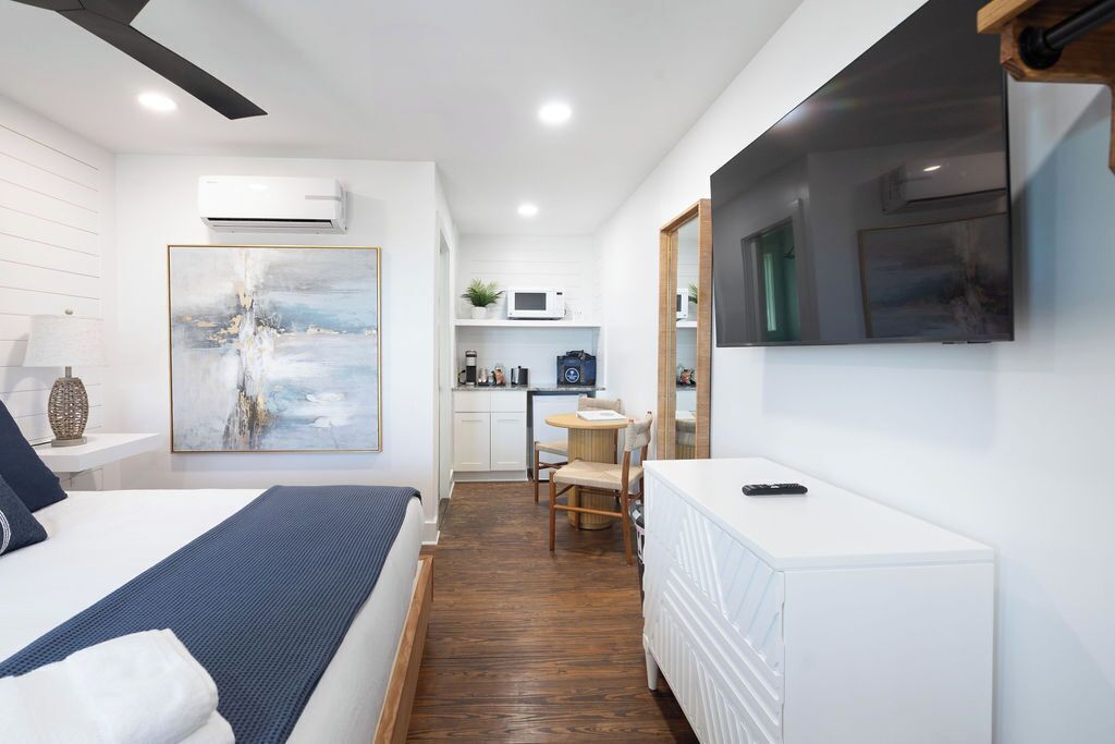 A hotel room with a bed, a desk, a chair, a TV, and a kitchenette.