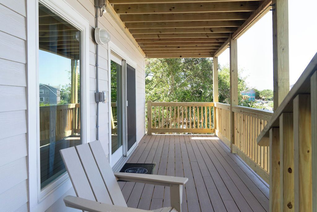 Una terraza de madera con barandilla, una silla y una puerta con ventanal.