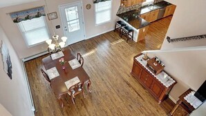 A spacious living room with a large gray sectional sofa, a dining area with a wooden table and chairs, and a kitchen with wooden cabinets and a granite countertop.