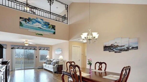 A spacious dining area with a wooden table and chairs, a chandelier, and artwork on the walls.