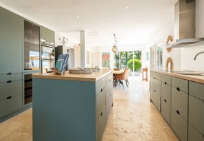 A modern kitchen with a central island, built-in appliances, and a dining area with a view. - Luxury sea view villa in Les Issambres | Villa Panorama Azur (Les Issambres)