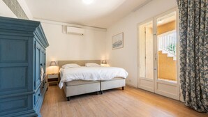 Un dormitori amb un llit, un taulell de nit, una petxera i una porta que dona a un balcó.