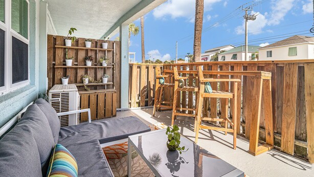Een overdekt terras met een houten schutting, een grijze bank en een kleine tafel met een plant.