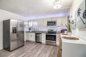 A modern kitchen with stainless steel appliances, white cabinetry, and a wooden floor. - Vacation Vibes Escape (Cape Canaveral)
