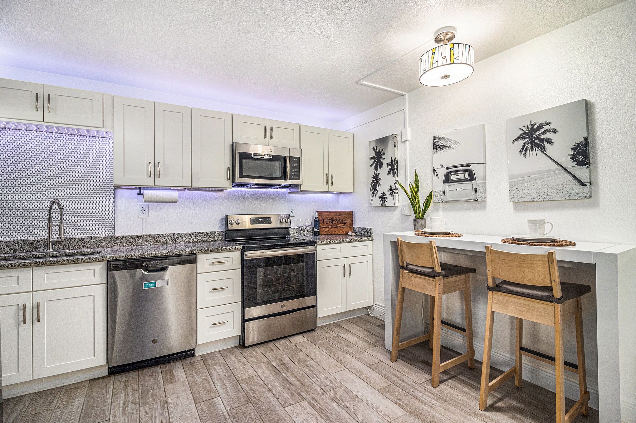 A modern kitchen with white cabinets, stainless steel appliances, a wooden countertop, and a bar area with two stools.