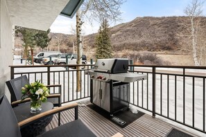A balcony with a grill, a table with chairs, and a vase of flowers.