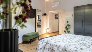 Ein modernes Schlafzimmer mit einem großen Bett, einer grünen Bank, einem an der Wand montierten Fernseher und einer Tür zu einem Essbereich.