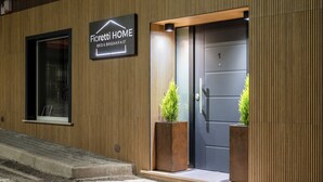 Ein moderner Hotelzugang mit einem Schild, das 'Fiorietti HOME BED & BREAKFAST' zeigt, einer dunklen Tür und zwei Pflanzgefäßen mit Grünpflanzen.