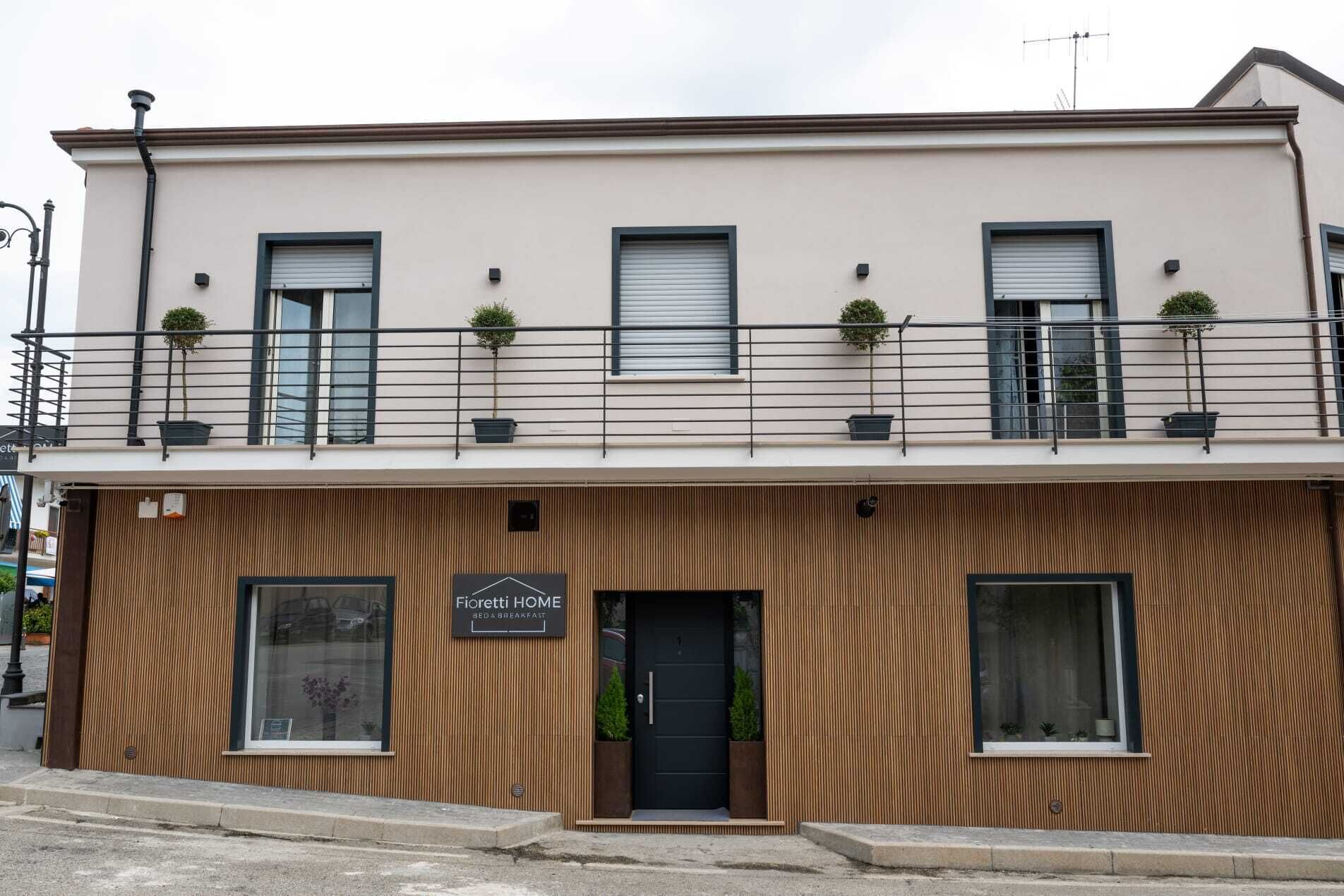 Ein zweigeschossiges Gebäude mit Holzfassade, einem Schild mit der Aufschrift 'Fiorietti HOME BED & BREAKFAST' und Balkonen mit Blumentöpfen.