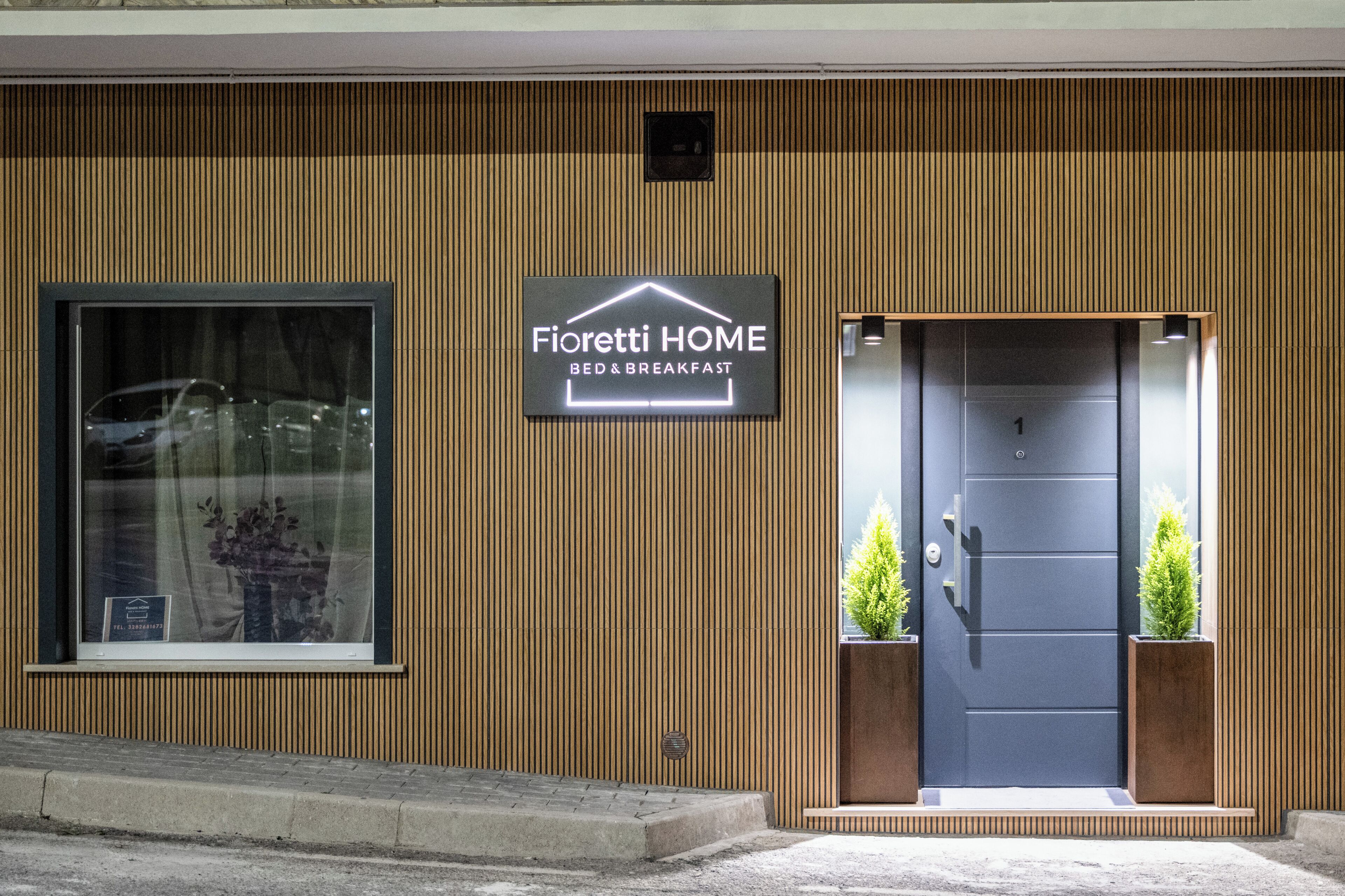 Un edificio con un letrero que dice 'Fioretti HOME BED & BREAKFAST', un ventanal grande y una puerta adornada con dos macetas.