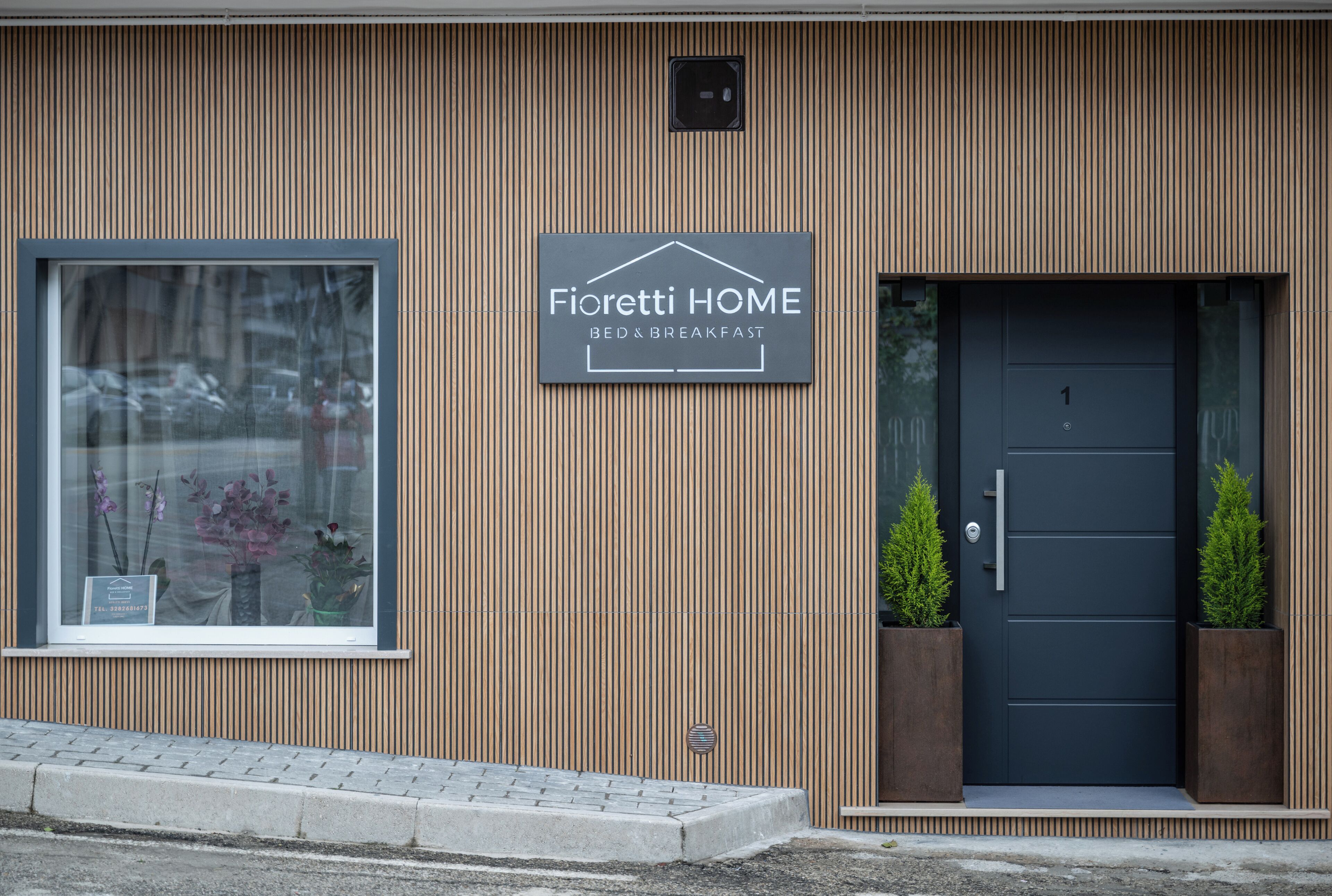 Un edificio con un letrero que dice 'Fioretti HOME BED & BREAKFAST', una ventana con flores y una puerta oscura con dos macetas.