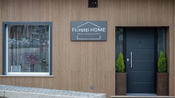 Un edificio con un letrero que dice 'Fioretti HOME BED & BREAKFAST', una ventana con flores y una puerta oscura con dos macetas.
