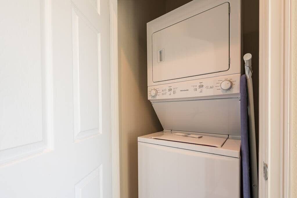 A compact laundry room with a front-loading washer and dryer, a door, and a towel rack.