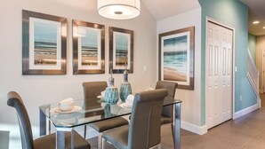 A dining area with a glass table, chairs, and framed artwork on the wall. - 3BR Home w/ Private Pool Near Disney (Clermont)