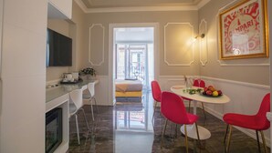 Una cocina moderna con televisión, armarios blancos y un comedor con sillas rojas y una mesa preparada para dos.